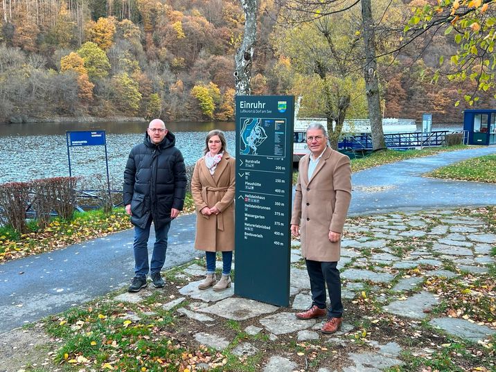 Hochwertig anmutend und informativ führt ein neues Leitsystem durch die touristischen Orte am Rursee: Einruhrs Ortsvoreher Christoph Poschen, die Tourismus-Beauftragte Damaris Schönewald und Bürgermeister Bernd Goffart stellten die neuen Stelen und Fahnenwegweiser vor. Foto: T. Förster